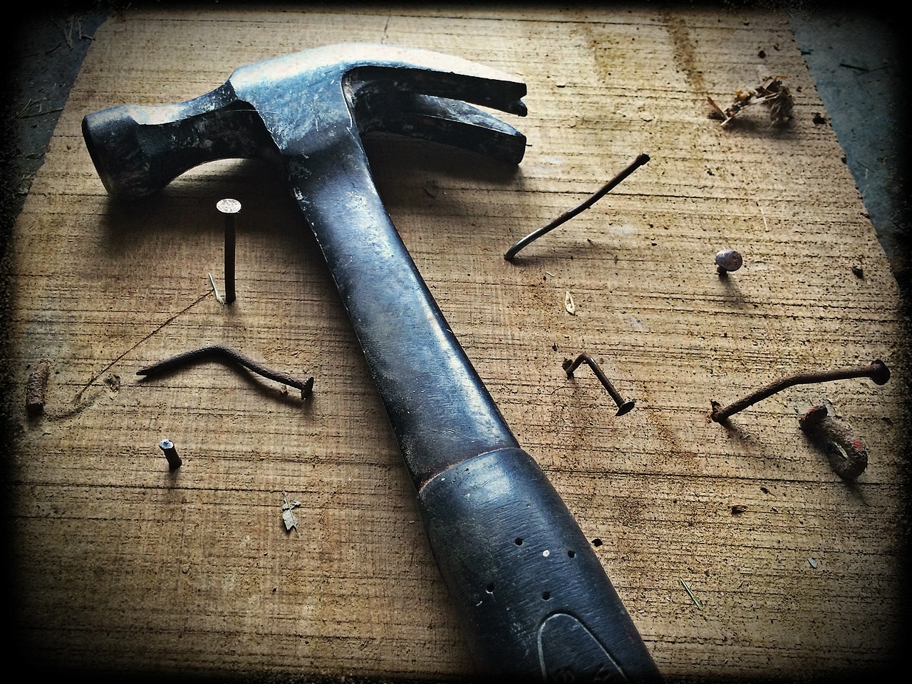 A claw hammer and scattered nails on a weathered wooden board