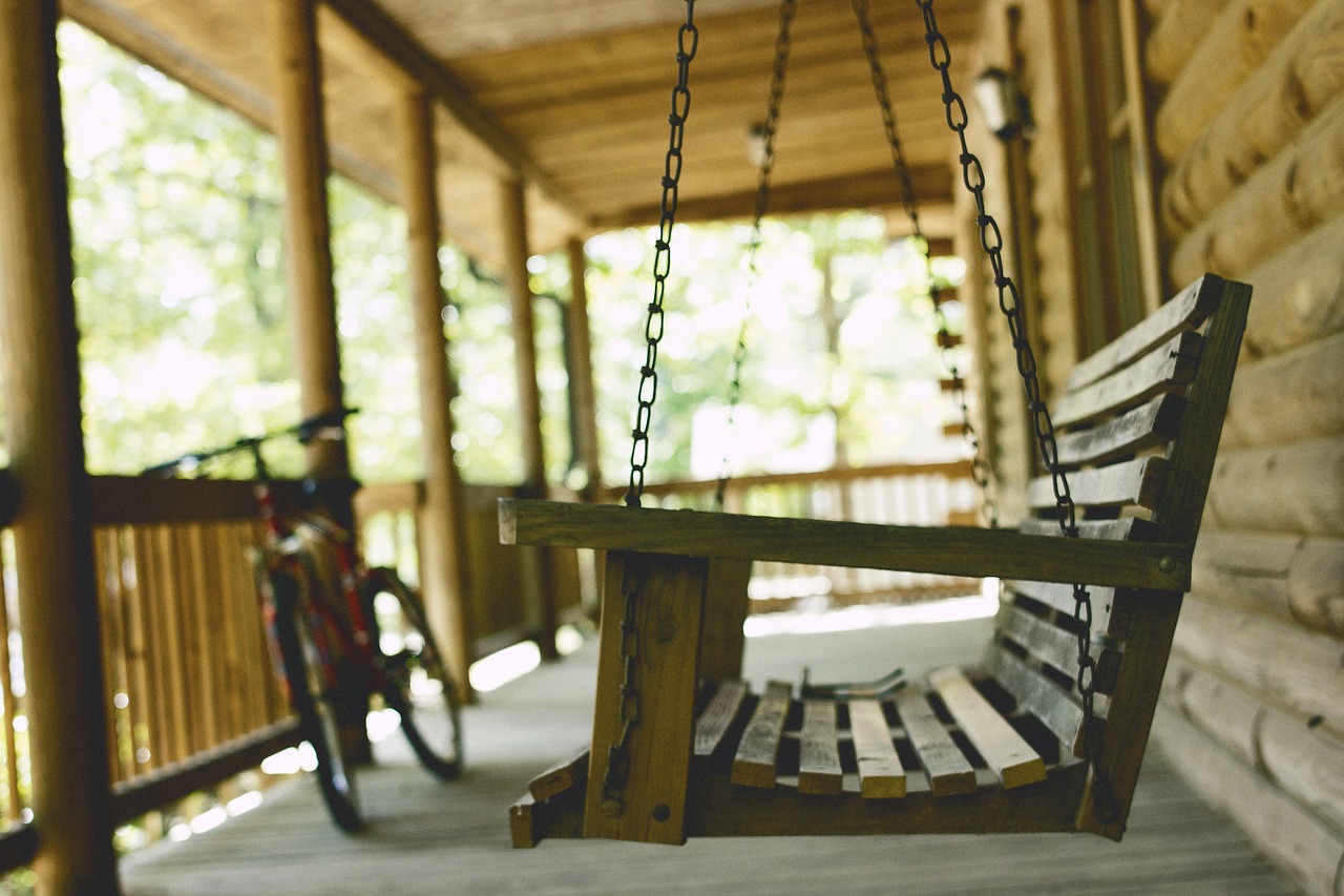 A wooden porch swing hanging from chains beside a bicycle against a log cabin wall